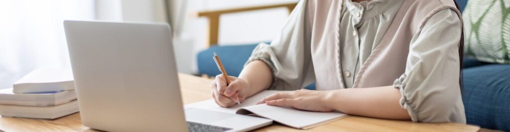 Woman reading from a laptop and writing notes.